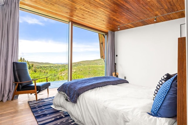 bedroom with wood-type flooring, floor to ceiling windows, multiple windows, and wooden ceiling