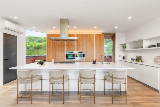 kitchen featuring a breakfast bar, white cabinets, a large island, exhaust hood, and a wall unit AC