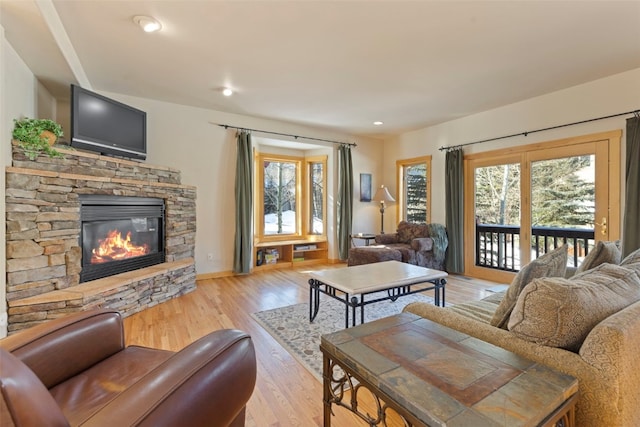 living room featuring a stone fireplace, light wood-type flooring, and a wealth of natural light