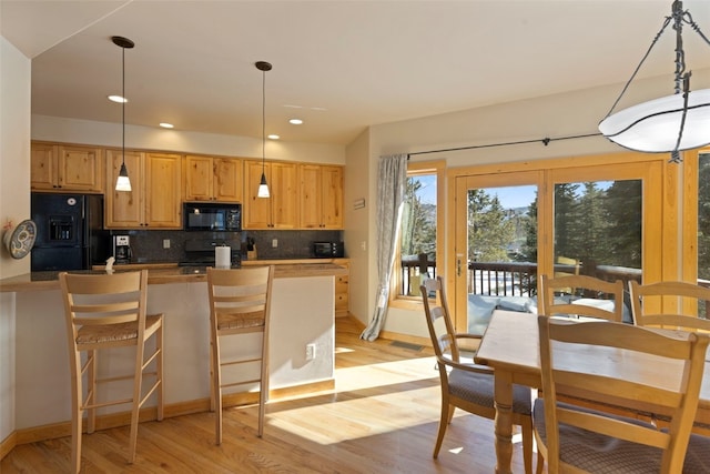 kitchen featuring a breakfast bar, pendant lighting, decorative backsplash, black appliances, and light wood-type flooring