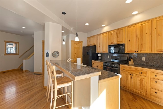 kitchen featuring tasteful backsplash, hanging light fixtures, a kitchen bar, and black appliances