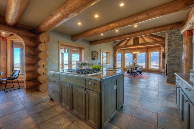 kitchen with rustic walls, vaulted ceiling with beams, stone countertops, stainless steel gas stovetop, and a center island with sink