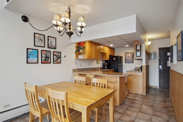 dining room with a chandelier, a textured ceiling, baseboard heating, and wooden walls