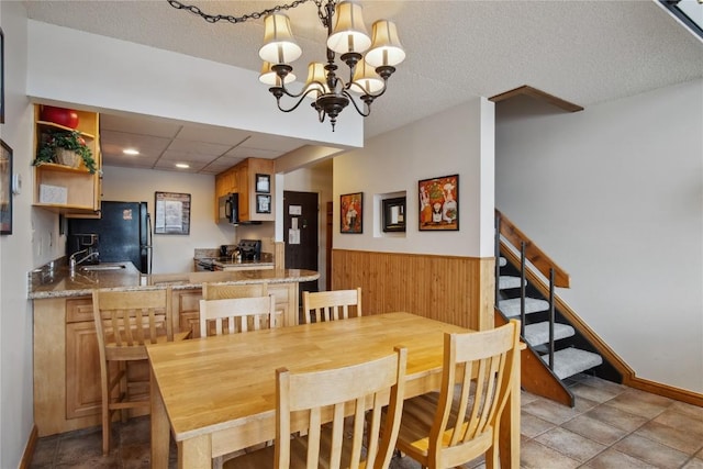 dining room with wood walls, sink, a textured ceiling, and a chandelier