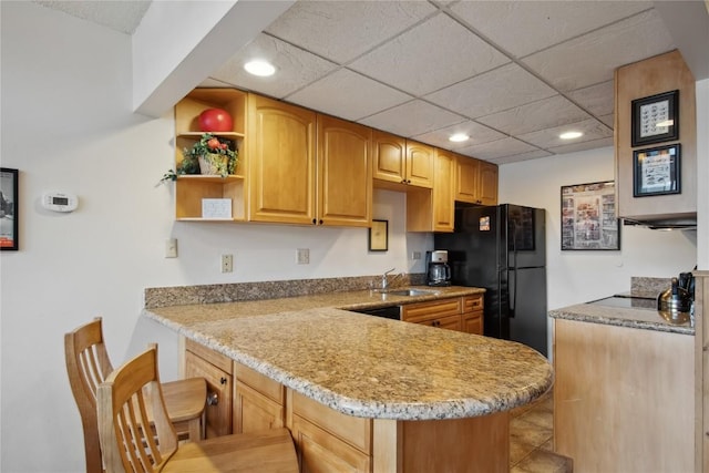 kitchen with kitchen peninsula, a drop ceiling, black refrigerator, and sink