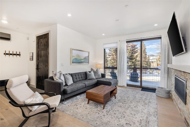 living area with an AC wall unit, light wood-type flooring, a glass covered fireplace, and recessed lighting