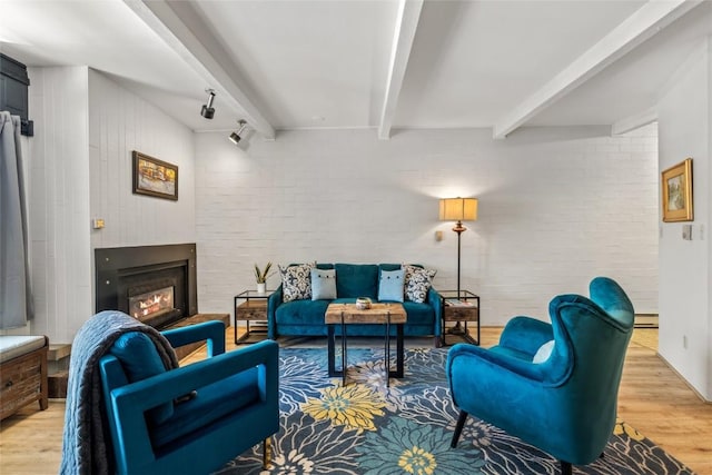 living area with a glass covered fireplace, beamed ceiling, wood finished floors, and brick wall