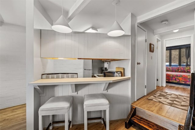 kitchen featuring pendant lighting, wood finished floors, brick wall, and a breakfast bar