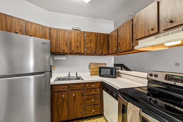 kitchen featuring under cabinet range hood, light countertops, appliances with stainless steel finishes, and a sink