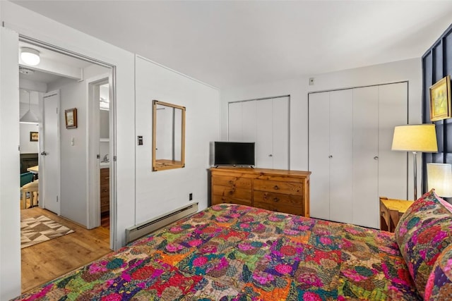 bedroom featuring two closets, a baseboard heating unit, and wood finished floors