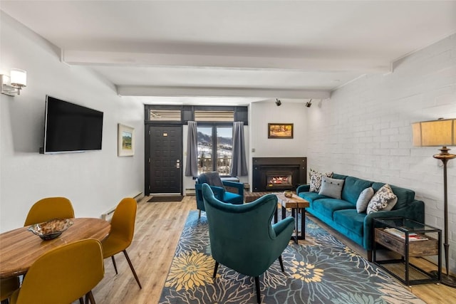 living area featuring beamed ceiling, light wood-style flooring, and brick wall