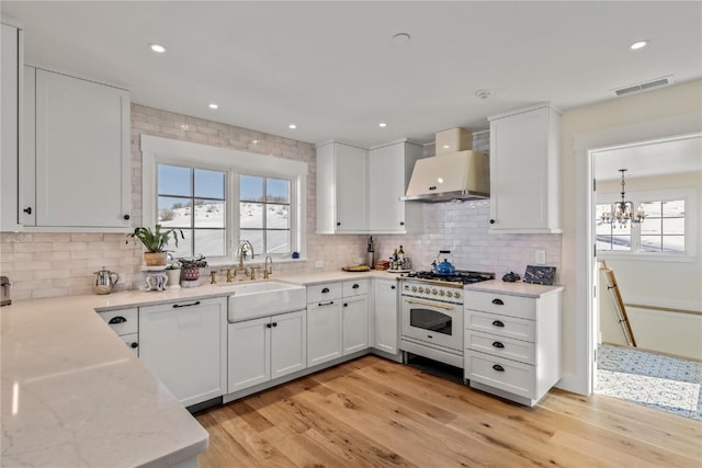 kitchen featuring wall chimney exhaust hood, sink, light wood-type flooring, high end white range oven, and white cabinets