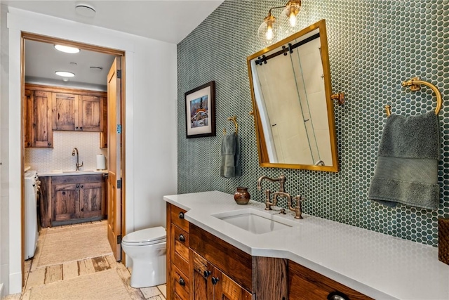 bathroom featuring vanity, toilet, washer / dryer, and backsplash