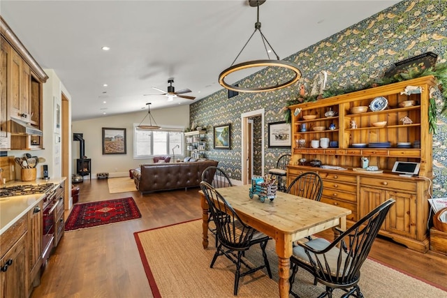 dining space featuring hardwood / wood-style flooring, ceiling fan, lofted ceiling, and a wood stove