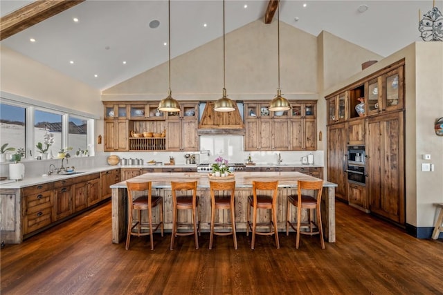 kitchen with a spacious island, custom exhaust hood, hanging light fixtures, dark hardwood / wood-style flooring, and beamed ceiling