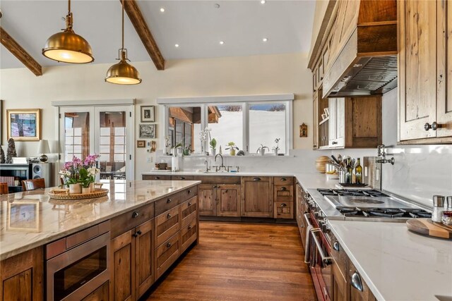 kitchen with sink, custom exhaust hood, light stone counters, decorative light fixtures, and appliances with stainless steel finishes