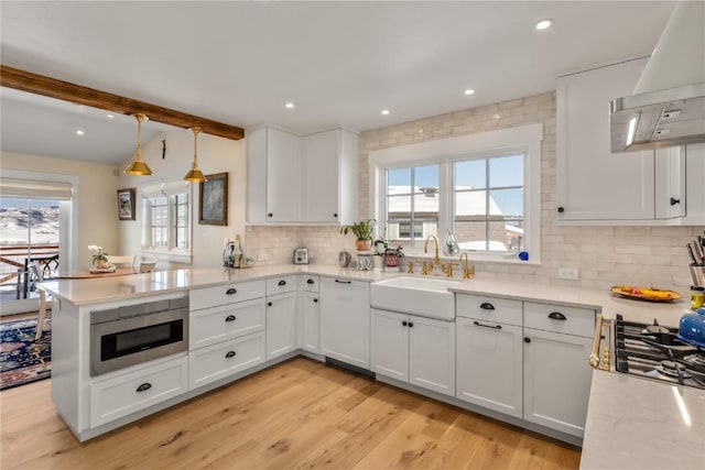 kitchen with hanging light fixtures, stainless steel microwave, kitchen peninsula, custom range hood, and white cabinets