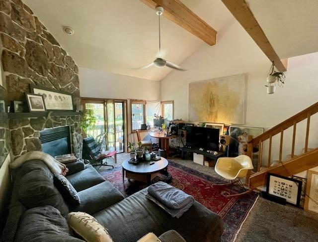 living room featuring beam ceiling, high vaulted ceiling, a stone fireplace, and ceiling fan