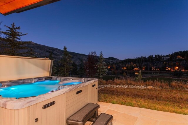 patio terrace at dusk featuring a mountain view and a hot tub