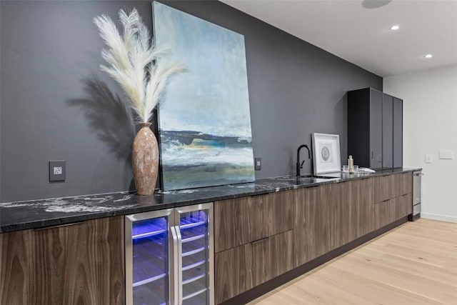 kitchen with wine cooler, sink, dark stone counters, and light wood-type flooring