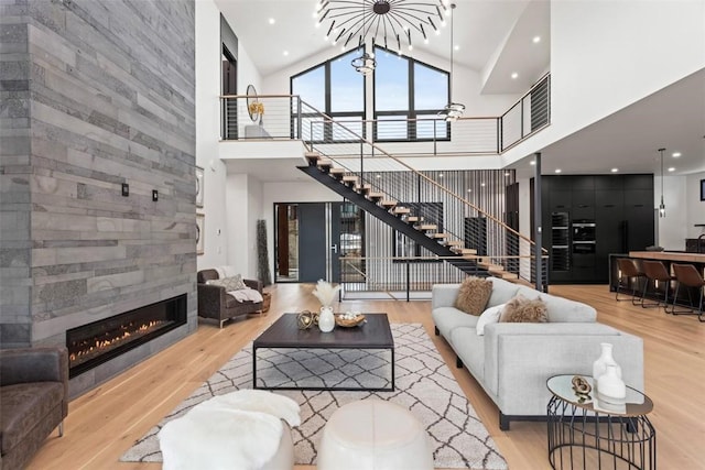 living room featuring a tile fireplace, light hardwood / wood-style flooring, high vaulted ceiling, and a chandelier