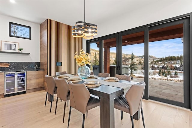 dining area with a mountain view, light hardwood / wood-style floors, an inviting chandelier, and beverage cooler