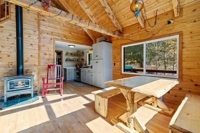 dining room featuring light wood-type flooring, beam ceiling, high vaulted ceiling, wooden ceiling, and wood walls