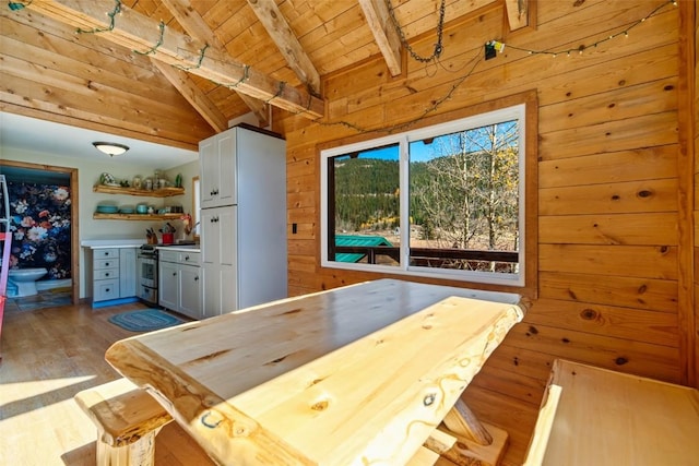 kitchen featuring beam ceiling, wooden walls, stainless steel stove, wood ceiling, and hardwood / wood-style flooring