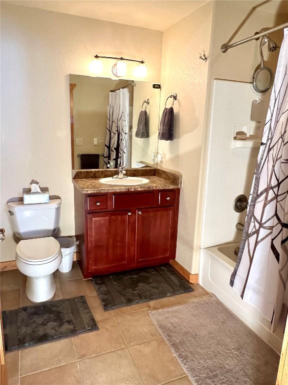 full bath with tile patterned flooring, toilet, vanity, baseboards, and shower / bath combo