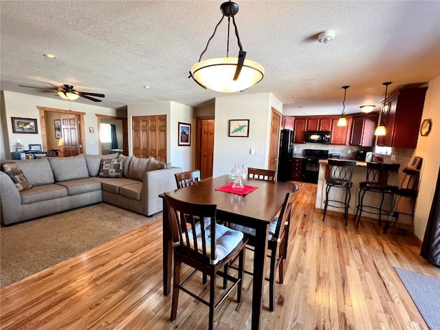 dining room featuring light wood-style floors, ceiling fan, and a textured ceiling