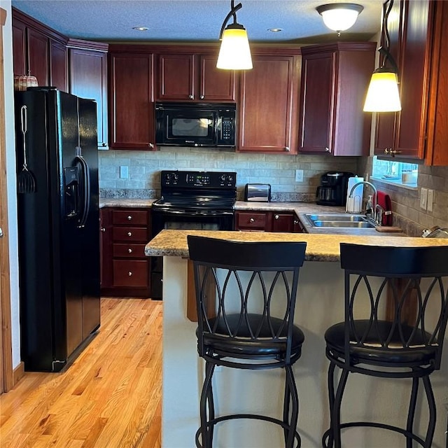 kitchen with light wood-style flooring, a peninsula, a sink, black appliances, and pendant lighting