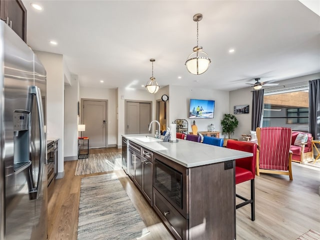 kitchen with stainless steel fridge with ice dispenser, dark brown cabinets, hanging light fixtures, and an island with sink