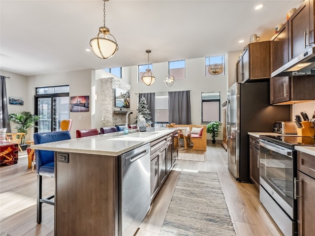 kitchen featuring appliances with stainless steel finishes, decorative light fixtures, a kitchen island with sink, dark brown cabinets, and a breakfast bar