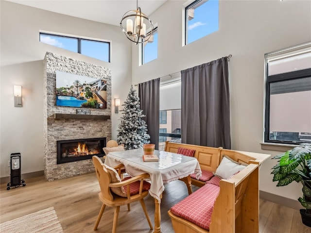 dining room with light hardwood / wood-style floors, a chandelier, a towering ceiling, and a stone fireplace