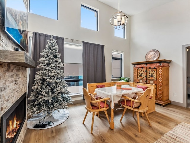 dining room with a towering ceiling, a notable chandelier, a stone fireplace, and light wood-type flooring