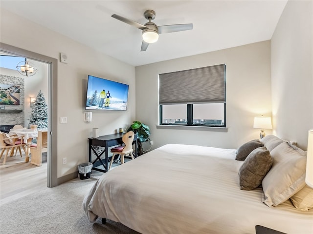 carpeted bedroom with a fireplace and ceiling fan with notable chandelier