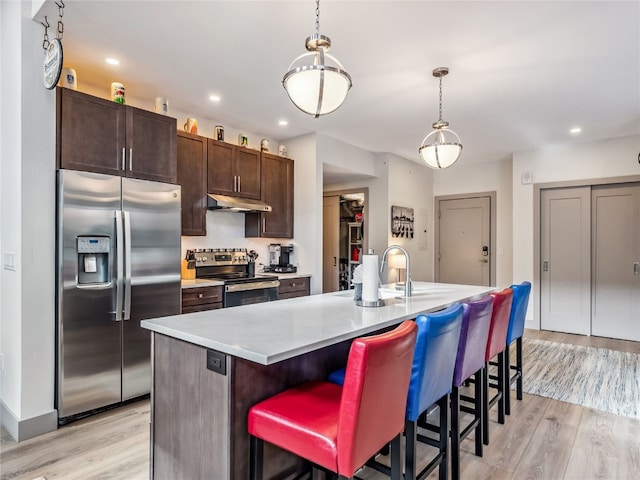 kitchen featuring hanging light fixtures, a kitchen bar, appliances with stainless steel finishes, and an island with sink