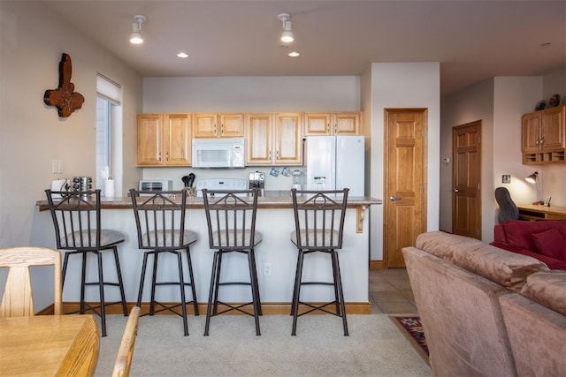 kitchen featuring white appliances, a breakfast bar, open floor plan, a peninsula, and recessed lighting