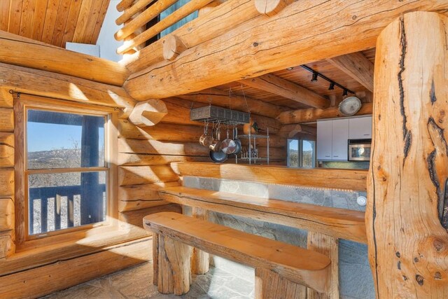 interior space with log walls, beamed ceiling, wooden ceiling, and rail lighting