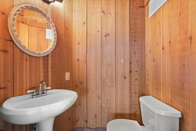 bathroom with wood walls, a sink, and toilet