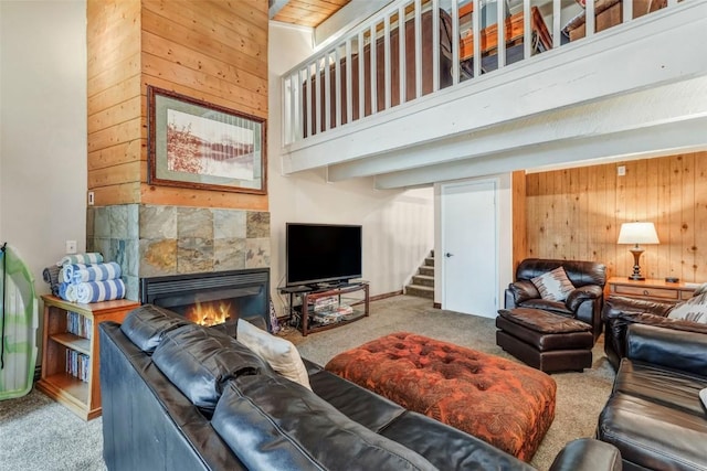 living room featuring a tile fireplace, carpet floors, a high ceiling, and wooden walls