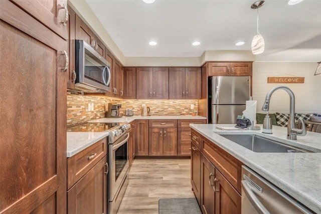 kitchen with pendant lighting, sink, tasteful backsplash, light stone counters, and stainless steel appliances