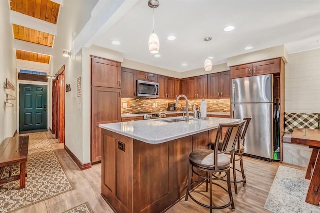 kitchen with sink, stainless steel appliances, an island with sink, pendant lighting, and light wood-type flooring