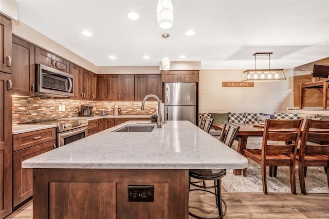 kitchen with a breakfast bar area, a center island with sink, stainless steel appliances, and decorative light fixtures