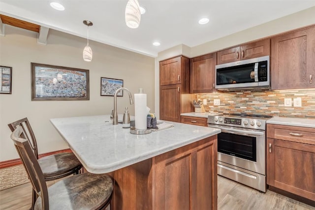 kitchen with hanging light fixtures, backsplash, a breakfast bar area, a center island with sink, and appliances with stainless steel finishes