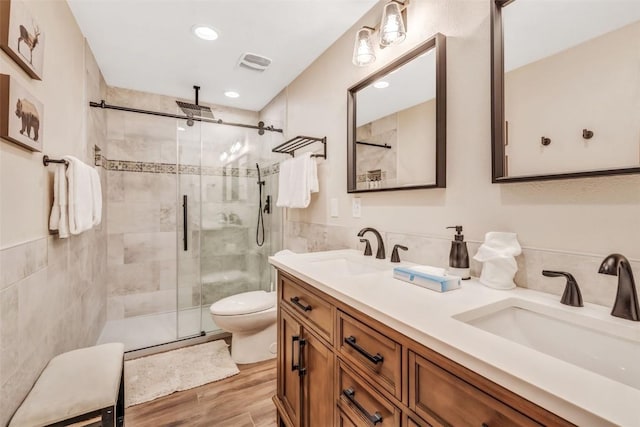 bathroom featuring vanity, a shower with door, hardwood / wood-style flooring, tile walls, and toilet