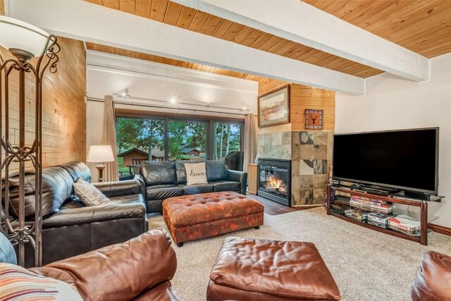 carpeted living room featuring wood walls, wood ceiling, beam ceiling, and a tiled fireplace