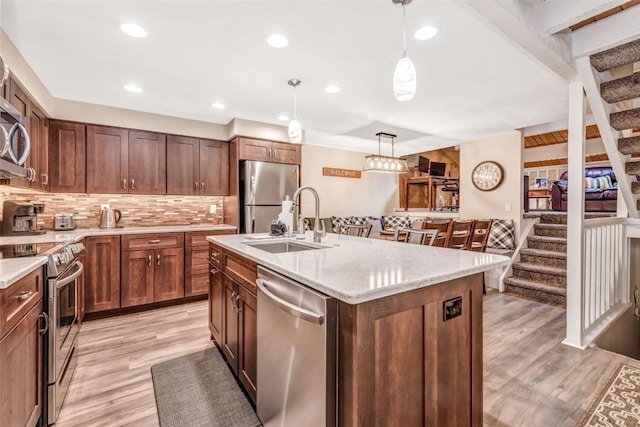 kitchen with a center island with sink, sink, light stone countertops, appliances with stainless steel finishes, and decorative light fixtures