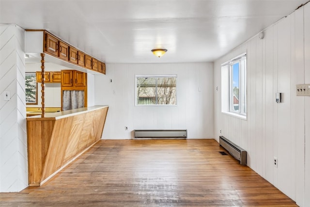 unfurnished dining area with baseboard heating, wood finished floors, a baseboard radiator, and a healthy amount of sunlight