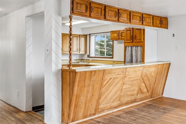 kitchen with a peninsula, a sink, wood finished floors, brown cabinets, and light countertops